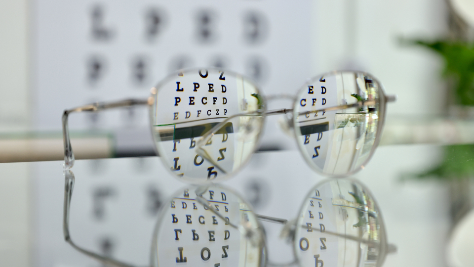 A pair of reading glasses on a table in front of an eye test chart